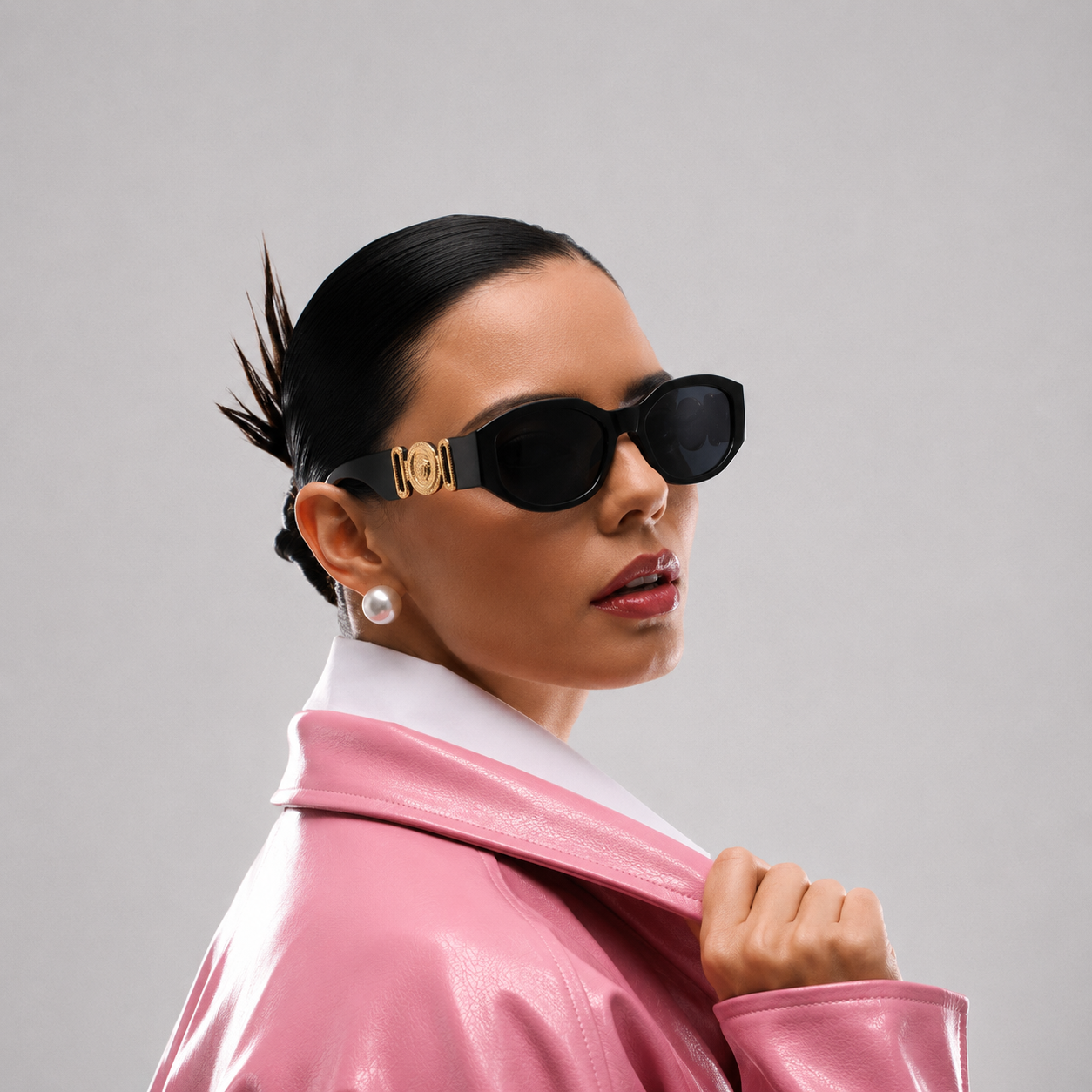 Woman wearing a pink jacket and black sunglasses with gold frames against a gray background