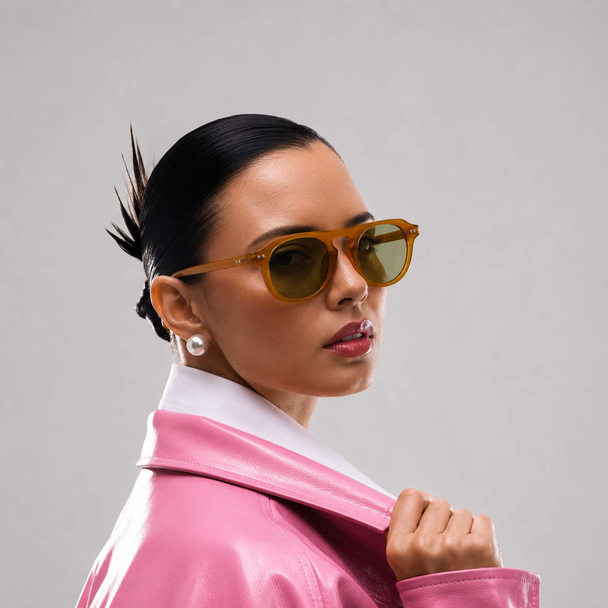 Woman wearing sunglasses and a pink jacket against a gray background