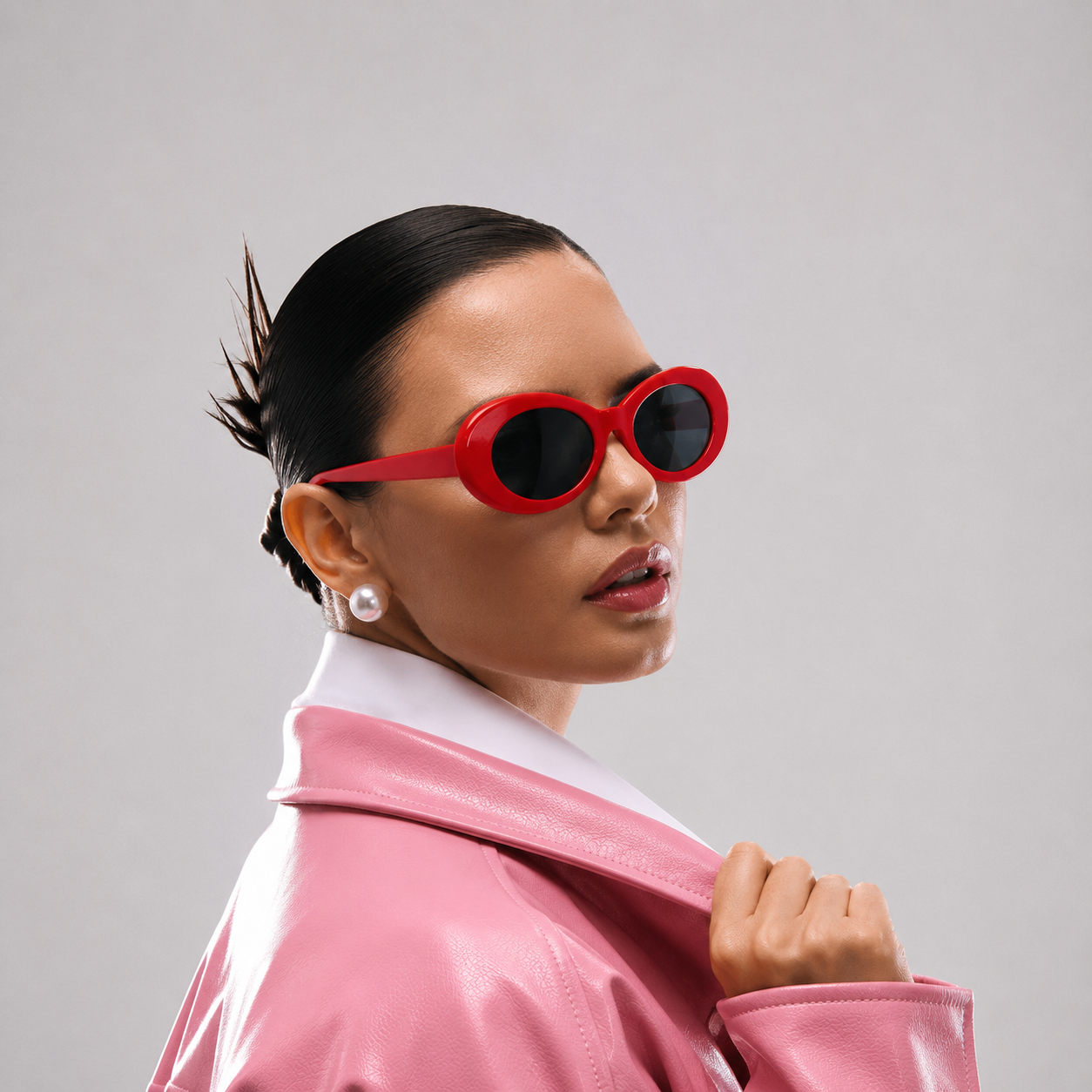 Woman wearing red sunglasses and a pink jacket against a gray background