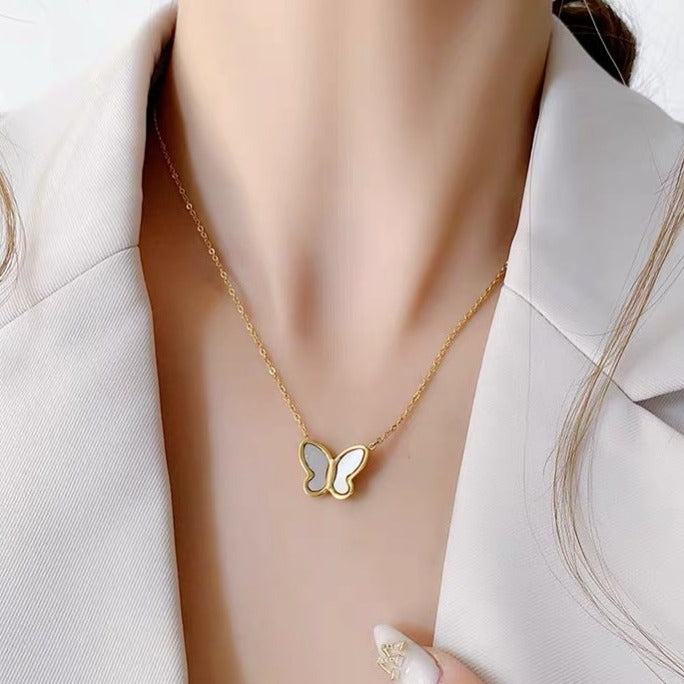 Gold butterfly necklace on a person wearing a white blazer