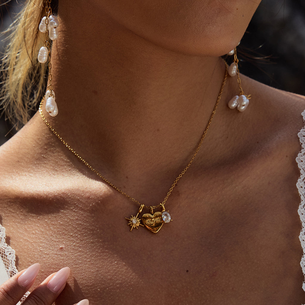 Close-up of a person wearing a gold necklace with a pendant, earrings, and a blurred background.