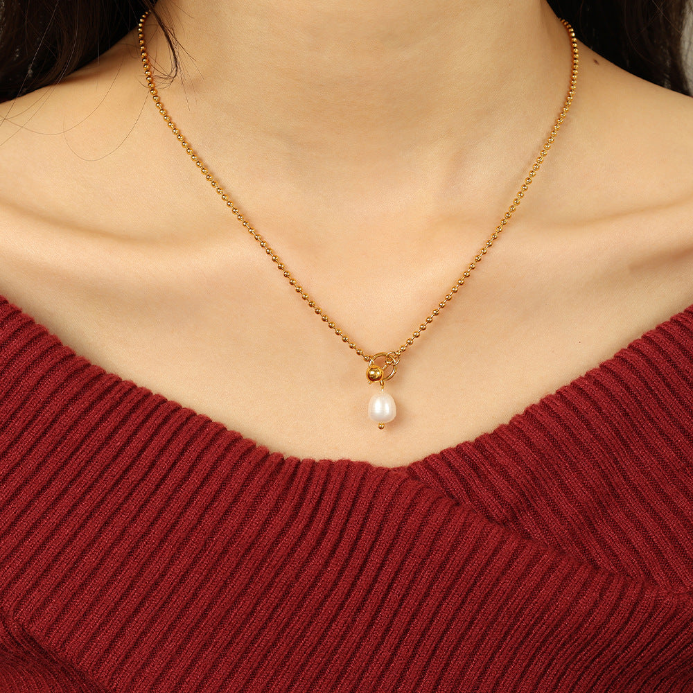 Gold necklace with a pearl pendant worn by a person in a red sweater.
