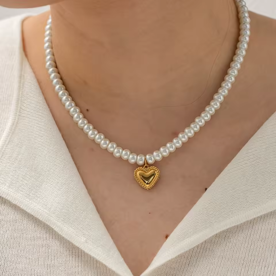 Pearl necklace with a gold heart pendant worn by a person in a white outfit.